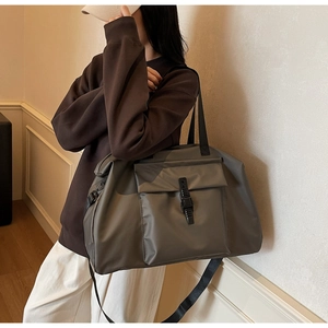 Side view of large grey travel bag with buckle detail on model in casual wear