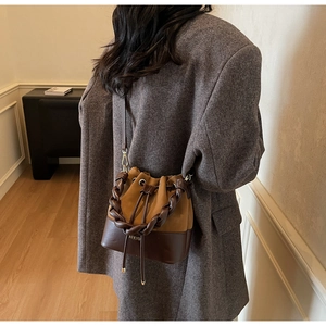 Detail view of contrast leather bucket bag with woven handle on grey coat model