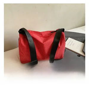 Detail showing red checkered fabric texture and black wide strap on minimalist shoulder bag
