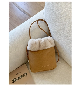 Close-up of brown suede bucket bag featuring beige faux fur trim and embossed logo detail