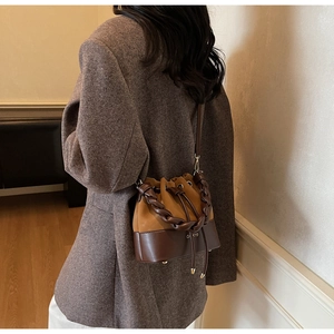 Detail of a brown leather bucket bag with braided handle and adjustable shoulder strap
