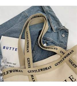 Vista piatta dettagliata della borsa tote in tela beige con logo Gentlewoman e giacca di jeans