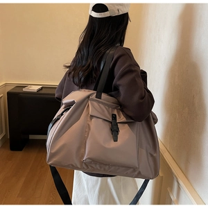 Detailed side view of a large taupe travel tote bag with black buckle pocket and strap