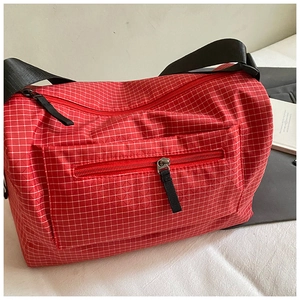 Detail of red plaid nylon crossbody bag with zipper pockets and black webbing strap