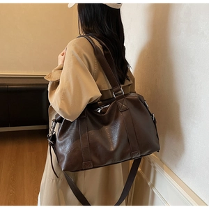 Detail of a large dark brown leather travel tote showing handles and texture on a model