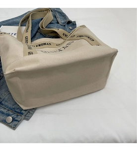 Dettaglio borsa tote in tela bianco sporco con tracolla logata su giacca denim