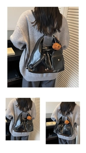 Detail of a large black glossy tote bag with multiple zippers and a plush bear charm