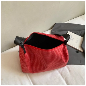 Detailed view of red textured checkered handbag with black woven handles and zipper