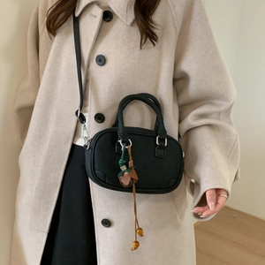 Detail of a black mini leather crossbody bag with floral charm worn on a wool coat