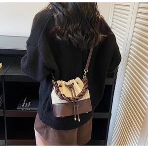 Detail of drawstring bucket bag with cream fabric and brown leather woven handle