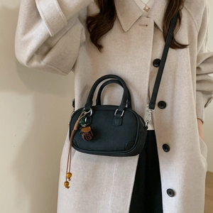 Detail view of black Boston bag featuring dual handles and a woven pinecone charm