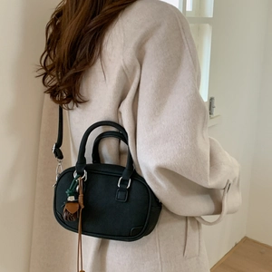 Close-up of black matte Boston bag with woven tassel charm and wool coat contrast