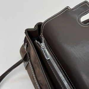 Detail of dark brown crossbody bag showing silver zipper and contrast stitching accents