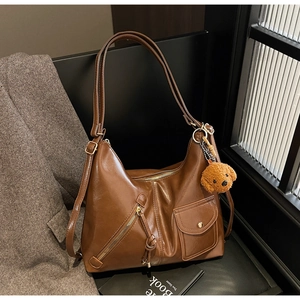 Detail of a brown leather Hobo bag with teddy bear charm on a black chair