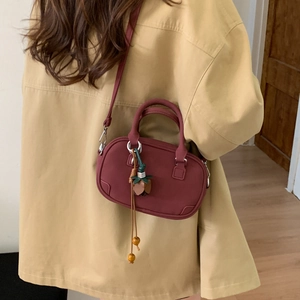 Detail of burgundy pillow-shaped handbag with woven rope bead charm on a beige trench coat
