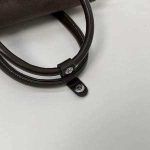 Close-up of the smooth leather handle and silver metal snap on the brown handbag