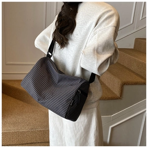 Detail of a chic black and white checkered cylinder bag worn by a model on stairs