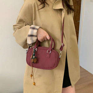 Detailed view of burgundy crossbody bag with round top handles and decorative charm detail
