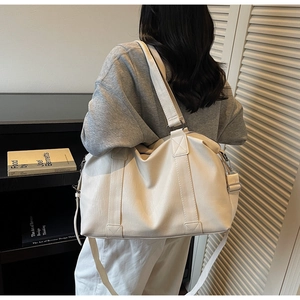 Rear view of model wearing a creamy beige PU leather travel tote with adjustable strap