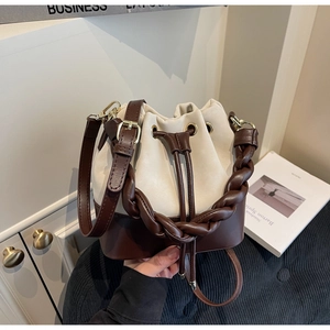 Detail of bicolor bucket bag showing braided handle and drawstring closure in warm indoor light