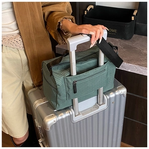 Detail of dark green checkered travel bag with sleeve fitting onto a silver suitcase handle