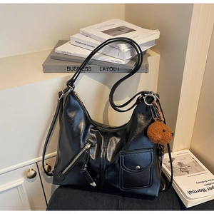 Detail of black glossy hobo bag featuring silver zippers and a cute brown plush bear charm