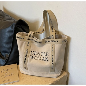 Primo piano della borsa tote in tela beige con scritta Gentlewoman nera su base in pietra