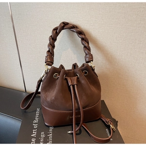 Detail of dark brown drawstring bucket bag with braided handle and suede patchwork