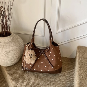 Dettaglio di una borsa tote vintage marrone a pois con fiocco in pelle e charm a orsetto