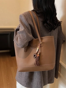 Classic brown pebble leather tote bag for women worn over shoulder with retro tassel charm
