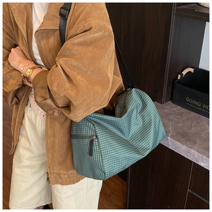 Detail of green checkered pillow bag with zipper closure on brown suede jacket outfit