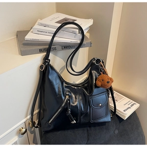 Detail of glossy black PU leather shoulder bag featuring side zippers and a plush bear charm