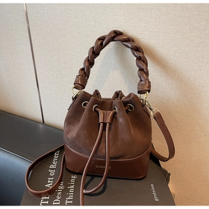 Detail of a dark brown bucket bag featuring woven handle and smooth leather texture
