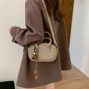 Detail view of khaki olive-shaped crossbody bag with decorative floral tassel on model