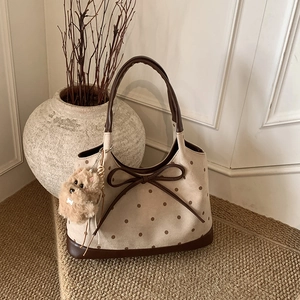 Dettaglio della borsa tote beige a pois con fiocco marrone e ciondolo a cucciolo