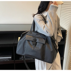 Detailed side view of a black large-capacity travel bag worn by a model in a modern room