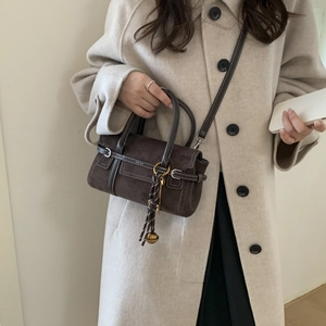 Detail view of brown suede handbag with white stitching and decorative gold ball knot charm