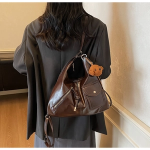 Detail view of a vintage dark brown shoulder bag with metal zippers and a plush bear charm