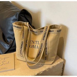 Dettaglio della borsa tote in tela kaki con logo nero su una base di pietra