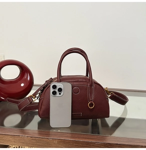 Close-up of burgundy pebble leather bowling bag with white stitching and gold hardware