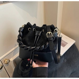 Close-up of black bucket bag with mixed textures, gold logo, and woven handle detail