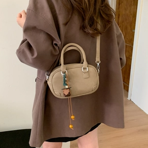 Detail view of khaki Boston bag with beaded charm on oversized brown blazer
