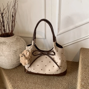 Dettaglio di borsa tote beige retrò a pois marroni con fiocco e ciondolo a forma di orso