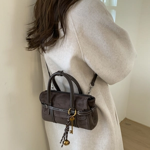 Brown suede crossbody bag with contrast stitching and charms shown on a model
