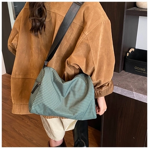 Back view of a green checkered crossbody bag worn by a model for a casual look