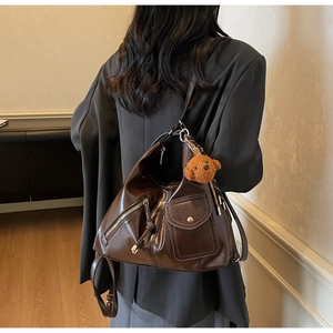 Detail of dark brown hobo bag with multiple pockets and a cute teddy bear charm