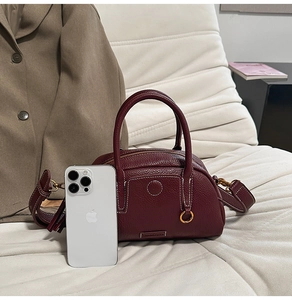 Close-up of burgundy litchi grain leather bowling bag with metallic logo and handles