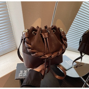 Brown leather bucket bag with woven handle and drawstring on a rustic wooden table