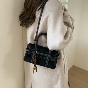 Detail of black suede square bag featuring white contrast stitching and a gold bell charm