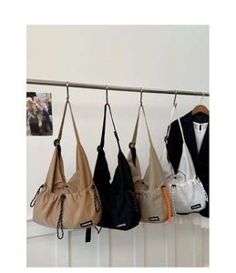 Row of large drawstring crossbody bags in four colors hanging on a metal rack in a studio